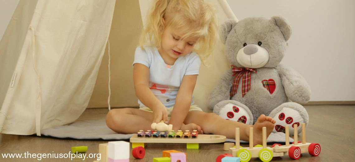 toddler girl playing xylophone with stuffed animal by her side
