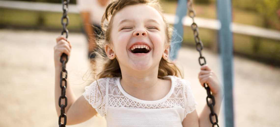 young pre-school aged girl smiling and playing on a swing