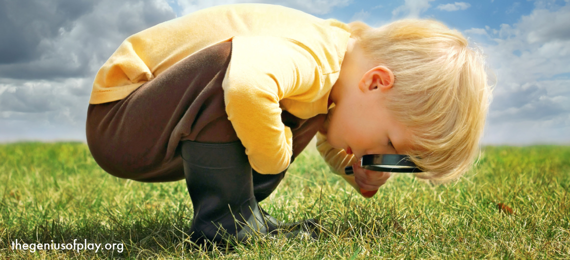 young blond boy exploring nature outside with a magnifying glass