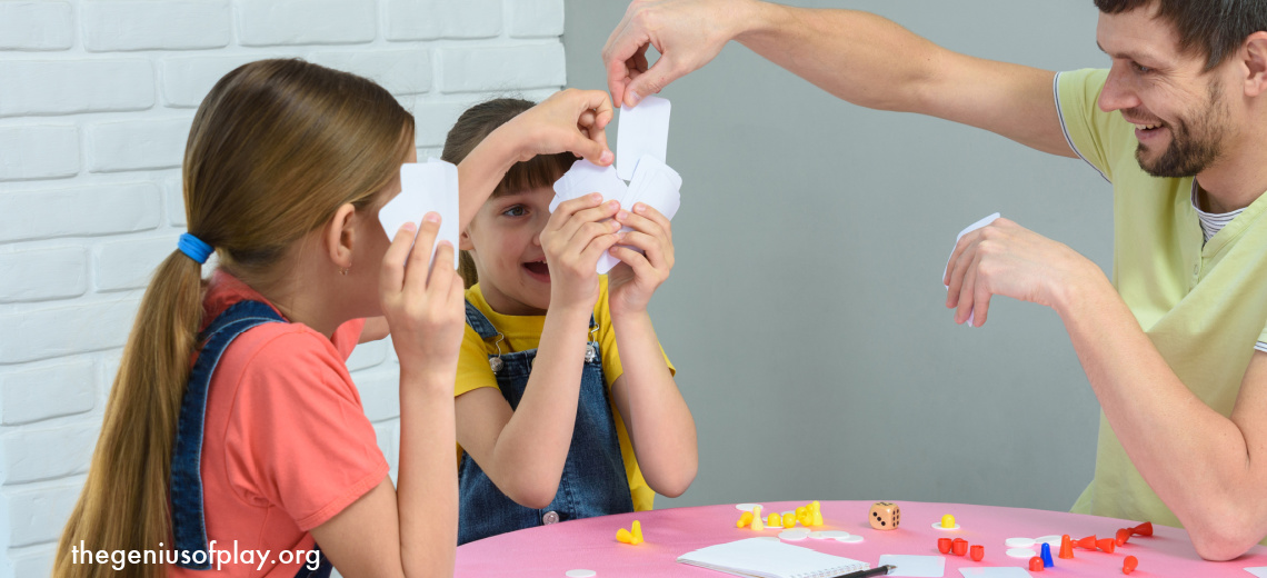 Dad playing a card board game with two young preschool and elementary age daughters