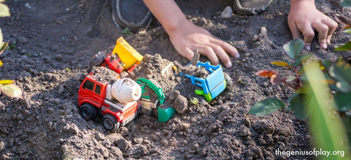 young children’s hands playing with toy trucks in dirt