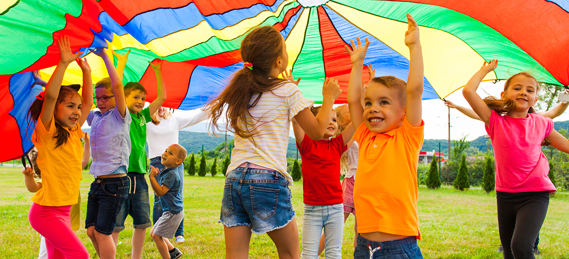 group of pre-school kids playing under a colorful parachute outdoors