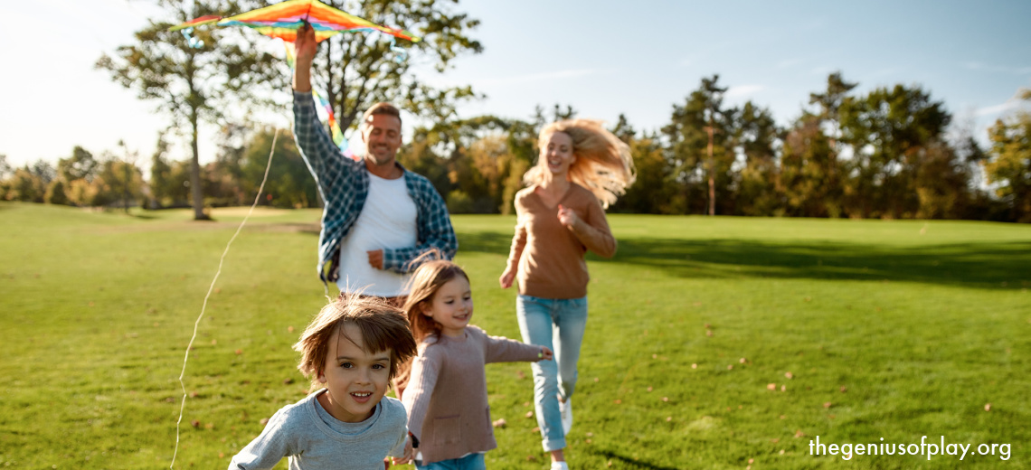mom, dad and two young kids all running outdoors while flying a kite