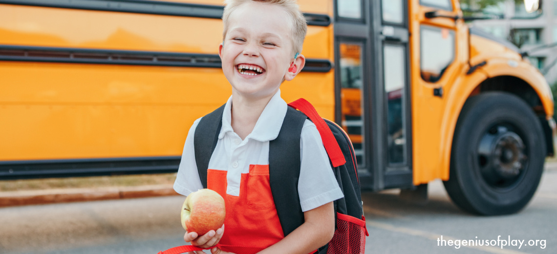 Happy laughing smiling Caucasian boy student standing by yellow school bus