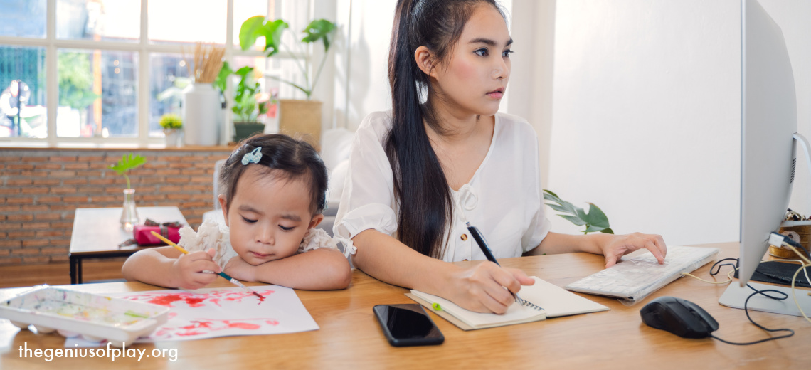 busy Asian mom working on home computer while young daughter is on coloring next to her