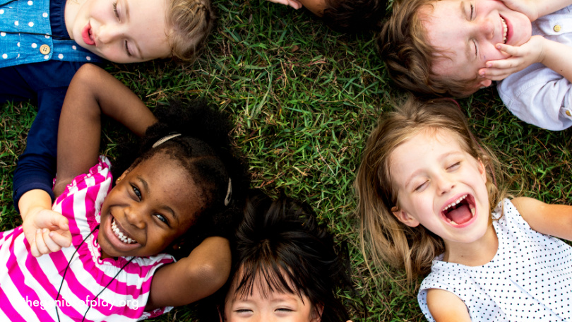 group of elementary aged kids lying on the grass outside and smiling