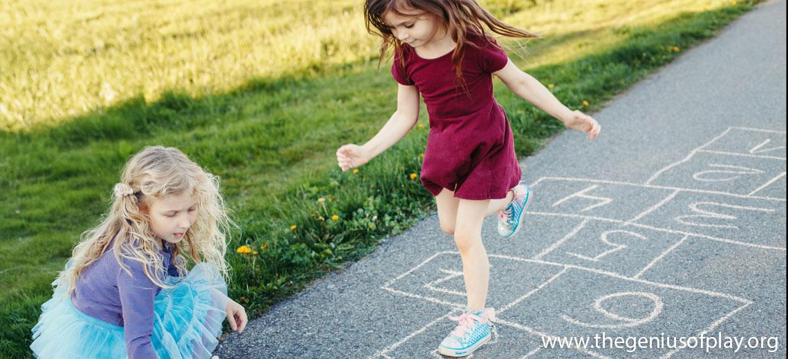 Two elementary aged girls playing hopscotch outdoors in a playground